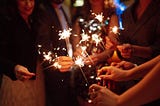 A group of friends’ hands hold out sparklers to welcome the new year.