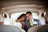 Interracial couple who look happy on their wedding day sit inside a car