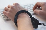 Someone’s hands using an Apple keyboard whilst wearing one single handcuff. (Absolutely ridiculous title image, but what can you really use to illustrate pre-orders locking you in?)