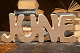 Wood carved into the word JUNE with two stacks of books behind it