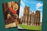 Two old guides for Wells Cathedral, showing a painted carving of a jester and the ornamental front facade of the church.
