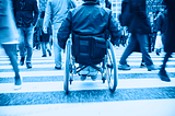 A person in a wheelchair using a crosswalk on a busy city street.