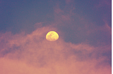 Light pink cloud surrounding an orange moon in the night sky