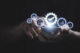 In the image, a pair of hands holds a smartphone from which a cascade of gear-shaped icons emerges, symbolizing different facets of digital services like analytics, user profiles, and settings, illustrating the concept of technology at one’s fingertips.