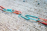 A connected chain of red and blue paper clips with one broken blue clip in the middle, which breaks the chain.