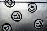 Social media icons including a smiley face, hearts, and thumbs up are painted in black and white on a metal surface.