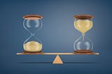Two hour glasses balancing on a teeter-totter against a navy blue background— one hourglass with sand flowing down from the top and one with sand already filling the bottom.
