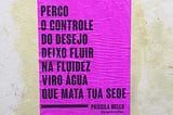 Lambe rosa choque colado na parede com os dizeres “Perco o controle do desejo  Deixo Fluir  Na fluidez viro água  Que mata tua sede” de Priscila Mello.