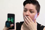 A woman staring at her phone in shock after hearing bad news.