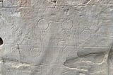 Multiple carvings of round objects with stick men standing behind them.