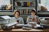 A seemingly introverted man and woman sitting and reading sitting in a room surrounded by books.