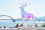 A statue of a deer on a ledge overlooking a body of water