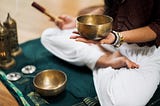 Woman sitting in meditation position with a singing bowl in her hand.