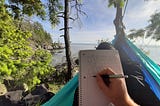 POV photo of a man lying in a hammock in a forest overlooking the ocean with a pen in his hand, writing a story.