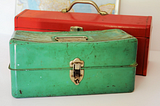 Photo of two colourful metallic toolboxes, a green one and a red one.