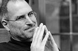 Photo of Steve Jobs, smiling and with hands tenting in front of him.