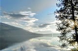 Serene lake, mountain, tree, and many beautiful clouds creating a mirror-like effect. An as above so below feeling.