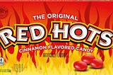 Movie theater-style box of Red Hots candy, reading “The Original Red Hots Cinnamon Flavored Candy,” with several candies against a background of cartoon flames.