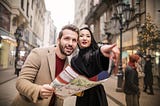 Man in brown suit with map standing beside woman wearing black coat and pointing