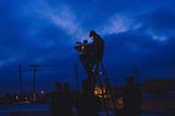 A camera operator sits on a stepladder against a blue night sky