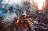 Smoke drifts into the air from a small fair set with a few branches and leaves.