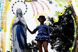young girl holds hand of Mother Mary statue.