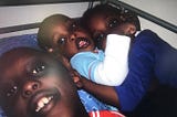photograph of 3 black kids next to each other on a bed look into the camera