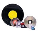 a photo of multiple items containing music, including a vinyl album, a cassette tape, a reel-to-reel tape, and a compact disc