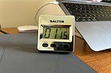 A timer made by Salter showing time being counted and has reached 1 minute 15 seconds. Behind it stands a laptop tilted on a stand. Image: Roland Millward