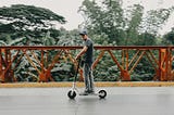 A man rides his electric scooter on a bridge.