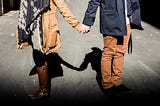 Couple wearing fall coats and boats holding hands on street