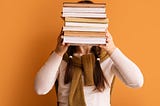 A woman holding a stack of books in front of her face.