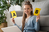 A photo of a young girl wearing headphones and holding up a sign saying A in one hand and a sign saying B in her other hand.