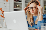 Woman holding temples with eyes closed and a stressed expression. A laptop is in front of her.