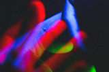 Hands intertwined, bathed in neon lights in blue, green, and red against a dark background