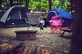 A camping ground set up with tents and chairs with a fire pit in the middle.