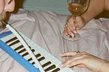 A couple plays a melodica together while drinking wine.