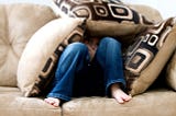 a person huddled under pillows on a sofa