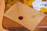 A lettter sealed in a brown envelope with a wax seal sits on a wooden desk