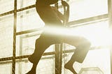 Fit barefoot man using only arm strength to pull himself up a rope in a gym