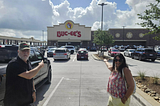 Two travelers stand outside a Buc-ee’s travel center in Texas, pointing toward the famous store that has become a surprising attraction for international visitors exploring America during the World Cup.