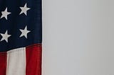 A segment of an American flag hanging veritcally on a white wall.