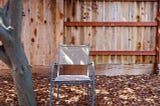 A chair in a back yard by a fence.