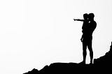 Black and white silhouette image, man holding child pointing to horizon.