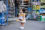 Little girl holding coin purse in front of store.