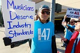 People holding banners saying “Musicians Deserve Industry Standards” and “Fair Treatment For All Musician”