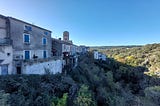 A stone village in france with a church tower. It sits on a hill overlooking a green valley.