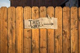 Wood sign on fence — reads ‘This way’ with an arrow