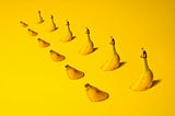 A row of bananas that have been cut and placed to look like they disappear through the surface on which they sit are place in a row, set against a yellow background. Representing the insights of Ramneek Bhoagl on the integration of chiropractic care and functional medicine.