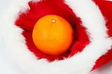 A large orange sits inside a red Christmas stocking with furry white trim.